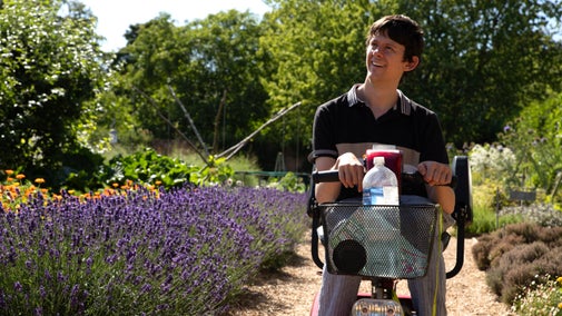 Visitor using a mobility scooter on a garden path bordered by lavender and colourful flowers in Felbrigg’s Walled Garden.